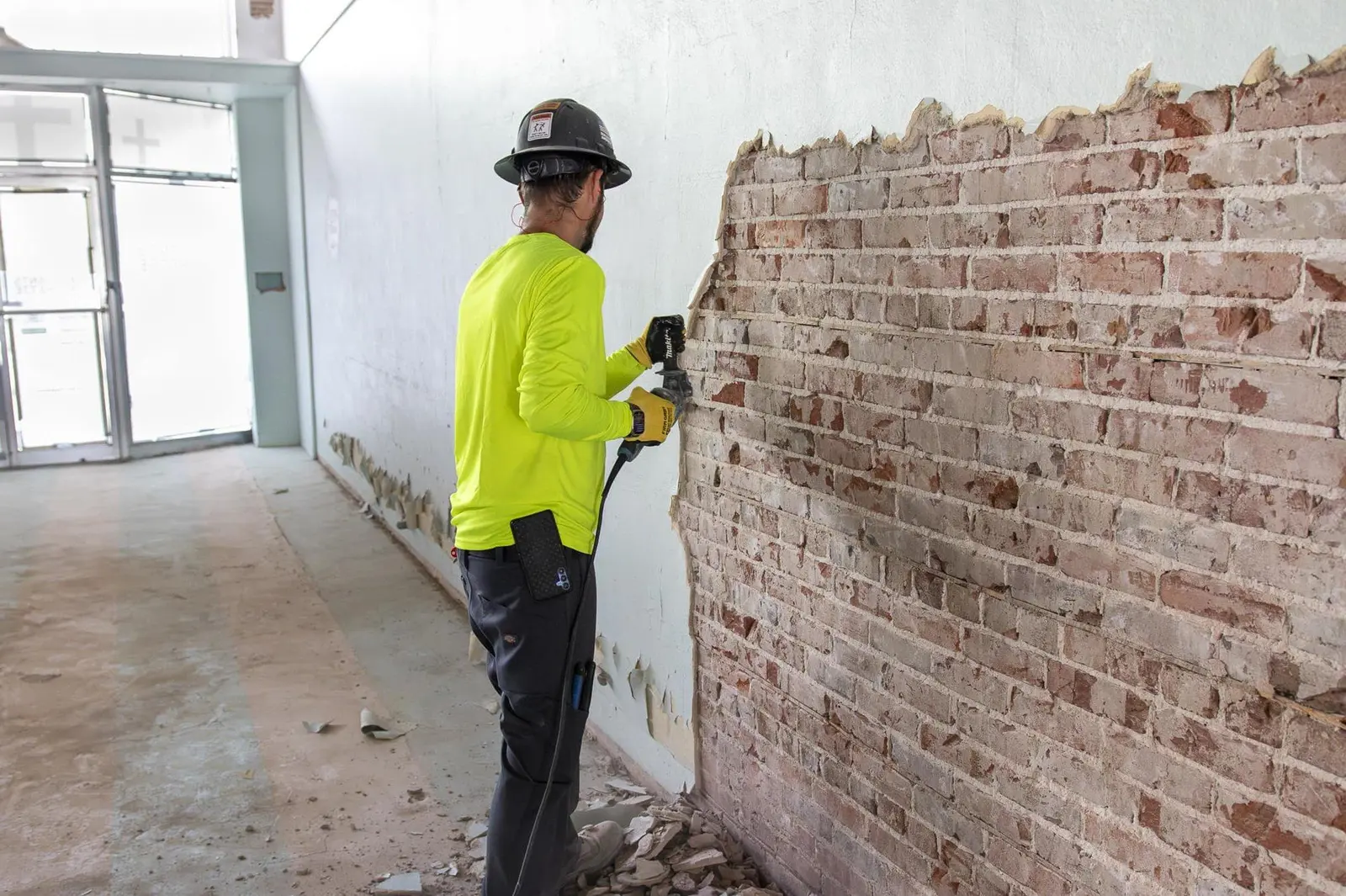 Worker removing plaster from an interior brick wall during selective demolition